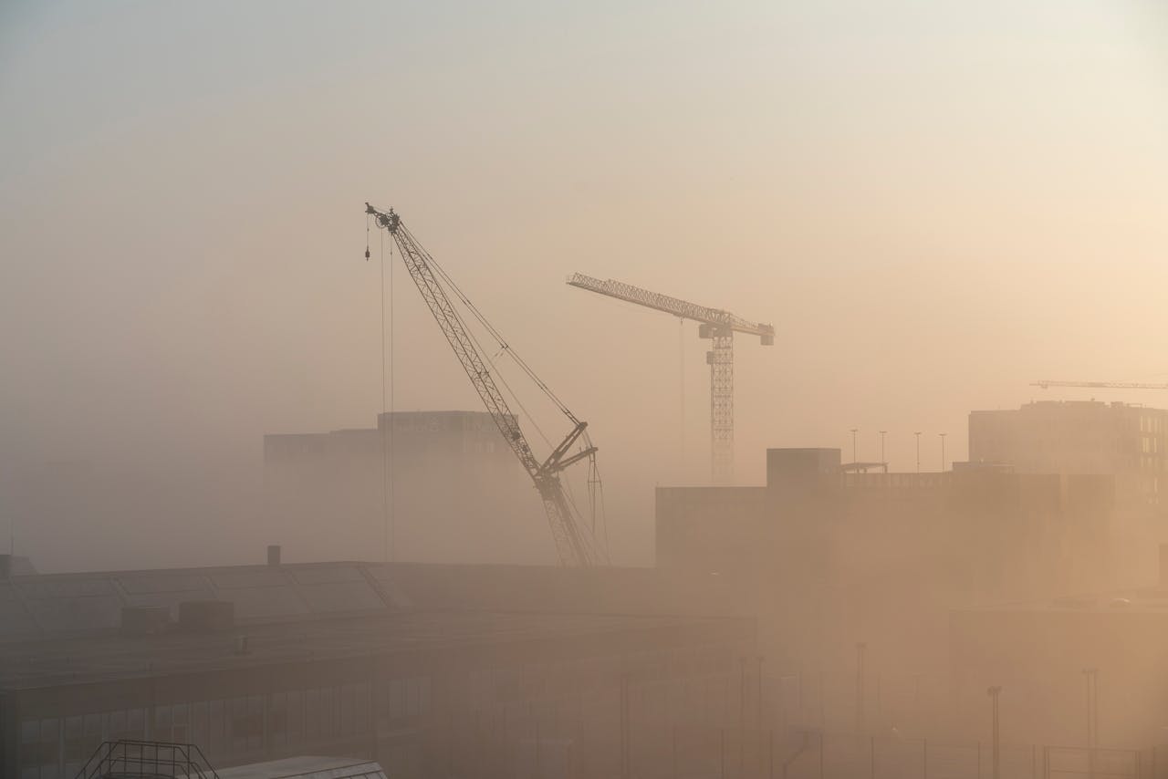Silhouetted cranes amidst fog at a construction site during dawn in Copenhagen.
